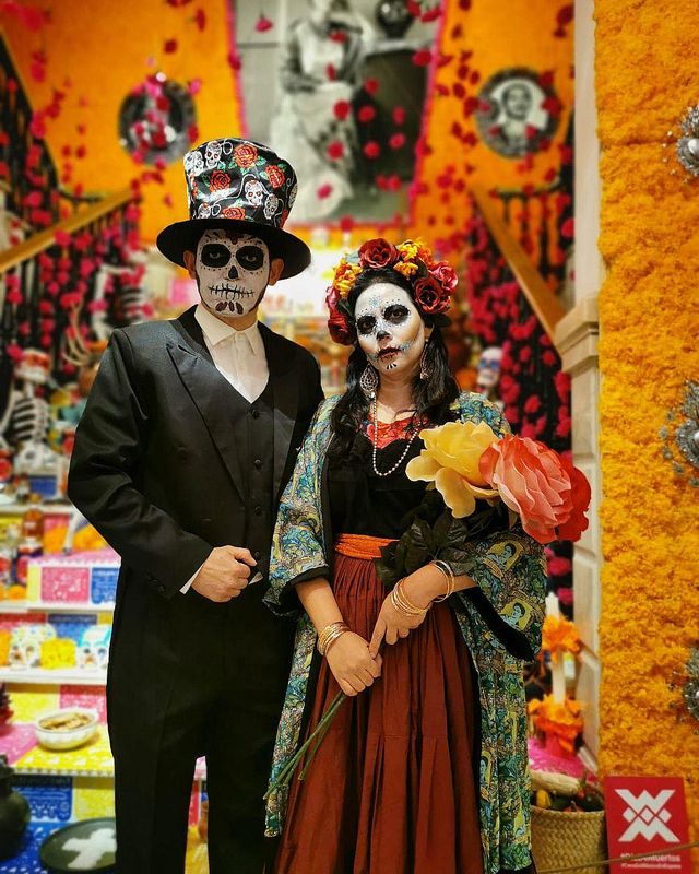 Una pareja vestida de catrín y catrina ante un altar de muertos