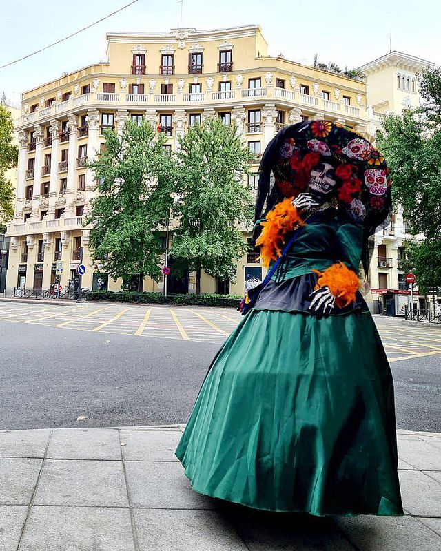 Una catrina con vestido verde y sombrero de flores en una calle de Madrid