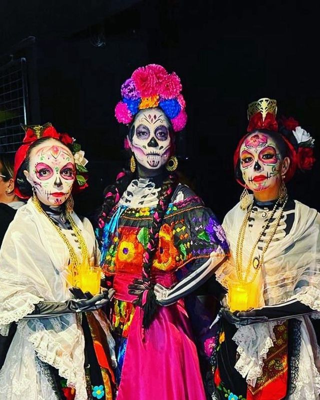 Tres catrinas con vestidos bordados y velas en las manos
