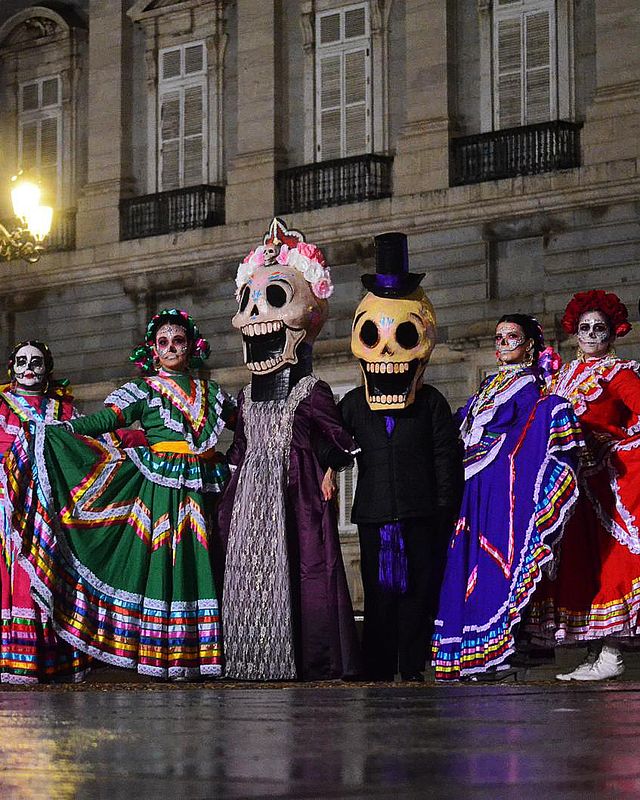Catrinas, mariachis y calacas gigantes posan de noche ante un palacio